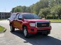 A red 2018 GMC Canyon pickup truck with a silver grille is parked with a truck bed cap and chrome wheels