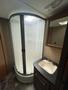 A bathroom area featuring a corner shower with a transparent curtain and a sink with two faucets on a dark countertop