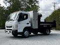 A 2015 Mitsubishi Fuso FE truck with a flatbed and a storage compartment attached to the side, featuring a white exterior and multiple orange lights on the roof