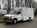 A white 2016 Chevrolet Express van with a boxy shape large side doors and multiple roof lights