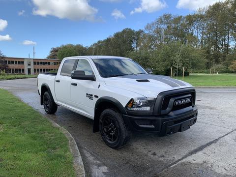 A white 2021 RAM 1500 with black accents and off-road tires parked at an angle showcasing its front and side design