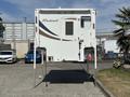 A 2018 Westland Travelaire trailer with a white exterior and decorative stripes is elevated on supports with a door and window facing forward
