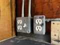 Two electrical outlets mounted on a wooden surface with metal conduits attached