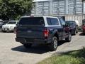 A blue 2015 Ford F-150 with a truck cap parked in a lot showing its rear and side view