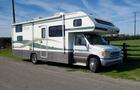 A 1998 Fleetwood Tioga Bunkbed recreational vehicle with a distinctive green and white striped design parked on a gravel road