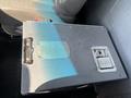 A metallic storage box with a latch and a lock sits on the floor of a vehicle with gray upholstery