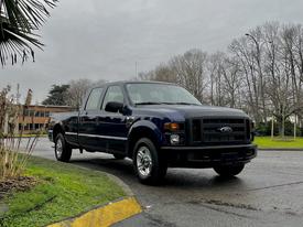 A blue 2008 Ford F-250 SD pickup truck with a four-door cab and chrome wheels is parked on the side of a road