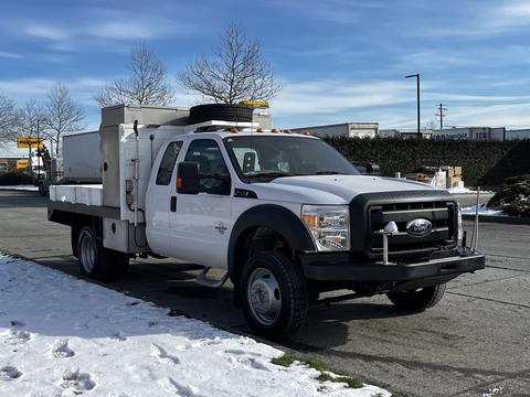 A white 2011 Ford F-450 SD truck with a flatbed and a storage unit mounted in the rear visible in the foreground