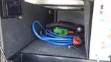 Inside the storage compartment of a 2021 Grand Design Recreational 311BHS with coiled blue hoses and various connectors arranged on a dark carpeted floor