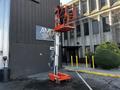 A 2000 JLG 12SP aerial lift with a raised platform and a worker standing on it, designed for reaching elevated areas