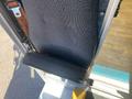 A black fabric seat from a 2012 Ford Econoline positioned at the entrance of the vehicle with visible wear and a metal latch attached
