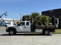 A 2012 Ford F-450 SD truck with a flatbed is parked with a load of potted palm trees in the truck bed