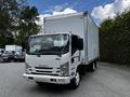 A white 2018 Isuzu NPR box truck is parked with a tall cargo box attached to its chassis and visible headlights and grille designed for commercial use