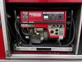 A red Honda EM 5000S generator with multiple control panels and outlets visible inside a compartment of a truck