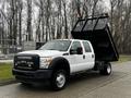 A white 2015 Ford F-550 dump truck with a black dump bed tilted upward and orange lights on the roof