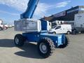 A 1997 Genie S-65 4X4 boom lift with a blue frame large tires and a raised aerial platform for lifting workers to high places
