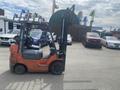 A red 2010 Toyota 7FGGU25 forklift with black forks parked on a lot surrounded by various vehicles