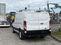 A white 2023 Ford Transit van with a roof rack parked in a lot showcasing its rear and side details