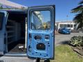 A blue 2008 Ford E-350 van with the side door open revealing the interior storage space