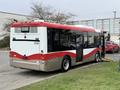 A 2016 Grande West Vicinity bus with a red and white design parked and showing the rear and side view with a lowered ramp for accessibility