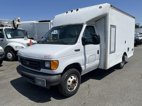 A white 2004 Ford Econoline with a boxy cargo area and a single side door parked among other vehicles