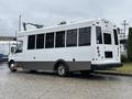 A white 2020 Chevrolet Express shuttle bus with large windows and a gray lower section is parked with its back facing the viewer