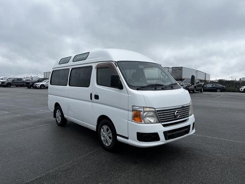 A white 2002 Nissan Van with a curved roof and large side windows parked on a lot