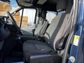 A 2017 Ford Transit interior featuring two gray fabric seats with upright backs and armrests on either side of the steering wheel