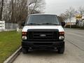 A 2011 Ford Econoline van with a white body and black grille parked on the street facing the camera