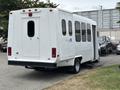 A white 2014 Ford E-350 shuttle bus with a rear entrance and multiple windows on the sides