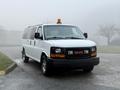 A 2016 GMC Savana van in white with a yellow light on the roof parked on a wet surface