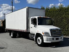 A 2021 Hino 338 box truck with a white cargo area and a silver front grille parked on pavement