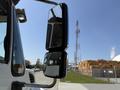 A side mirror of a 2009 International 7500 truck reflecting the view of the road and a telecommunications tower in the background