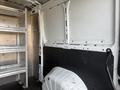 Interior of a 2017 RAM Promaster with metal shelving on the left and a large wheel well on the right against a white wall