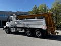 A white 2005 Volvo VND 122 dump truck with a yellow dump bed and a two-axle configuration parked with its side profile visible