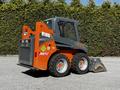 A 2017 Gehl R105 skid steer loader with an orange and gray design features a bucket attachment in the front and large rubber tires for mobility