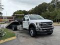 A 2022 Ford F600 tow truck in white with a flatbed and lights on top parked on a street