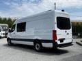 A 2019 Mercedes-Benz Sprinter van with a white exterior and black accents parked at an angle showcasing its side and rear views