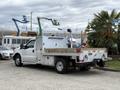 A white 2015 Ford F-350 Super Duty truck with a flatbed and toolboxes on the sides parked at a location with construction equipment visible in the background