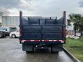 A 2015 Isuzu NPR HD truck with a flatbed and raised sides, viewed from the rear