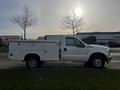 A white 2016 Ford F-350 SD with a utility truck bed and side storage compartments is parked with the sun setting in the background