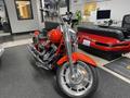 A 2024 Harley Davidson Fat Boy motorcycle with a glossy red body and chrome accents positioned prominently in an indoor setting