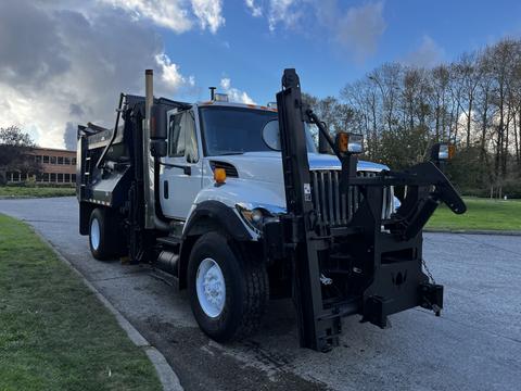 A white 2011 International 7300 truck with a black front-mounted snow plow and side-mounted equipment for snow removal