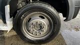 A close-up of a black Michelin tire mounted on a silver rim with multiple holes, featuring the tread pattern of a large truck tire