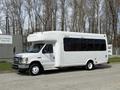 A white 2010 Ford Econoline bus with large side windows and a high roof is parked on a street