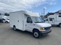 A 2004 Ford Econoline truck with a boxy white cargo area and a gray front bumper parked on a lot