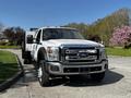 A 2016 Ford F-550 truck with a white exterior and black accents parked on a road, featuring large tires and a flatbed design