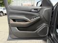 The interior door panel of a 2017 Chevrolet Tahoe featuring a black leather finish wood accents and controls for windows and locks