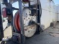 A close-up of a reel with red hoses mounted on a metal frame attached to a vehicle with visible bolts and fittings