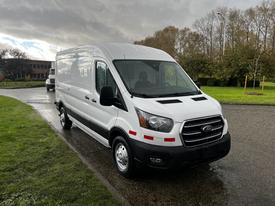 A white 2020 Ford Transit van with a high roof and a long wheelbase parked on a wet surface